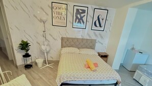 A modern bedroom with a bed, a bedside table, a floor lamp, a fan, and a potted plant.