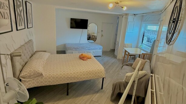 A bedroom with a bed, bedside table, and a mirror. There is a window with a view of the outside.