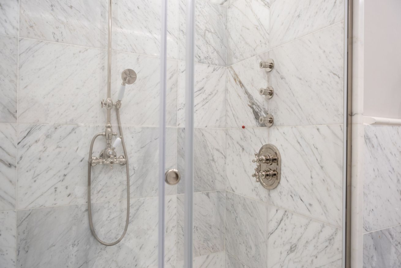 A shower with a handheld showerhead and a wall-mounted control panel.