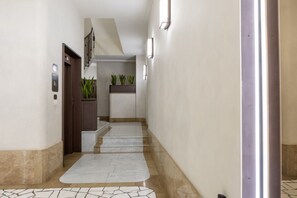 A hallway with a marble floor, a wooden door, and a staircase leading to an upper level.