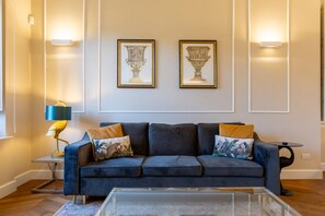 A modern living room with a dark blue sofa, two framed vases on the wall, and a lamp on a side table.