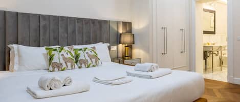 Ein ordentlich bezogenes Bett mit aufgerollten Handtüchern, einer Nachttischlampe und einem Kleiderschrank in einem Hotelzimmer.