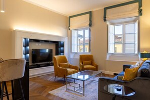 A living room with a TV, two armchairs, a sofa, and a glass coffee table. - Calzaiuoli Private House Silver (Firenze)