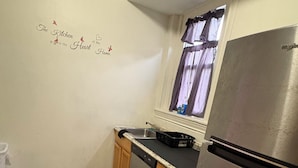 Eine kleine Küche mit einem Edelstahl-Kühlschrank, einem Fenster mit Vorhängen und einem dekorativen Wandschild.