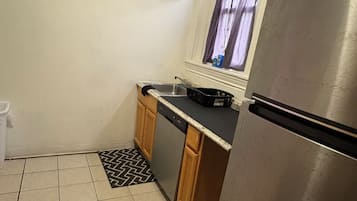 Eine kleine Küche mit einem Edelstahl-Kühlschrank, einem Fenster mit Vorhängen und einem dekorativen Wandschild.