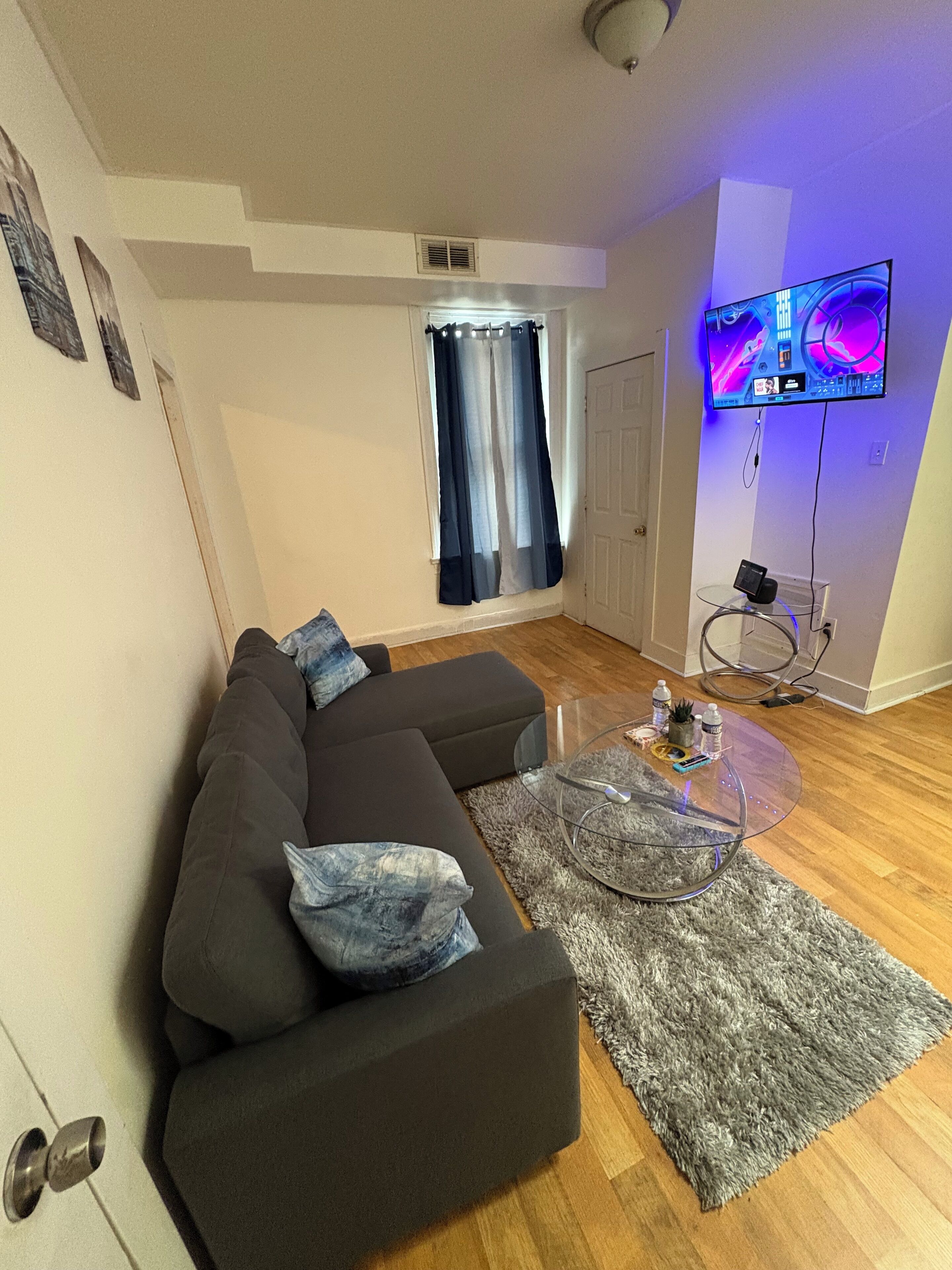 Ein modernes Wohnzimmer mit einem dunkelgrauen Ecksofa, einem Glastisch und einem flach an der Wand befestigten Flachbildfernseher.