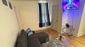 Ein modernes Wohnzimmer mit einem dunkelgrauen Ecksofa, einem Glastisch und einem flach an der Wand befestigten Flachbildfernseher.