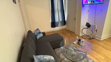 Ein modernes Wohnzimmer mit einem dunkelgrauen Ecksofa, einem Glastisch und einem flach an der Wand befestigten Flachbildfernseher.
