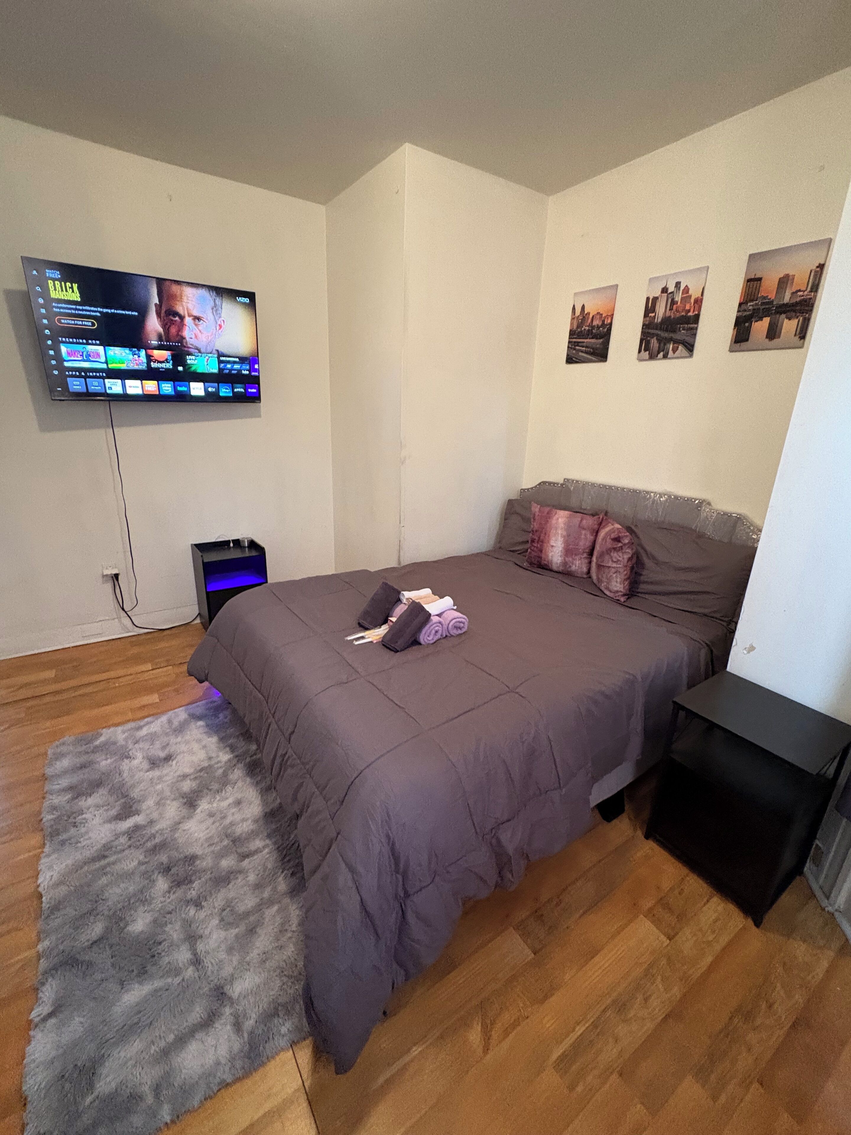 A bedroom with a bed, a TV mounted on the wall, a small table, and a rug.