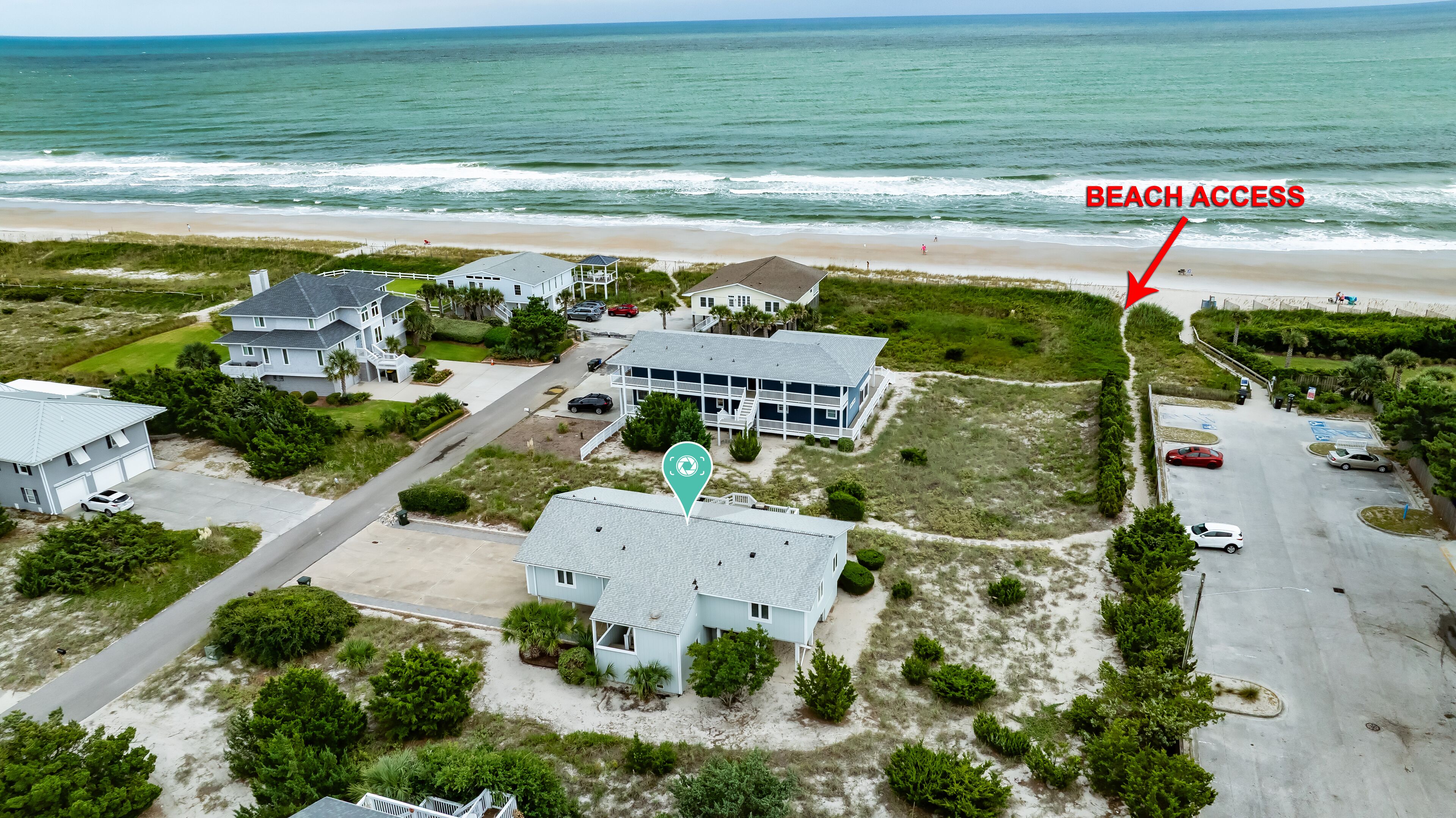 Vue aérienne d’un quartier résidentiel situé sur la côte, avec des maisons, un accès à la plage et un parking.