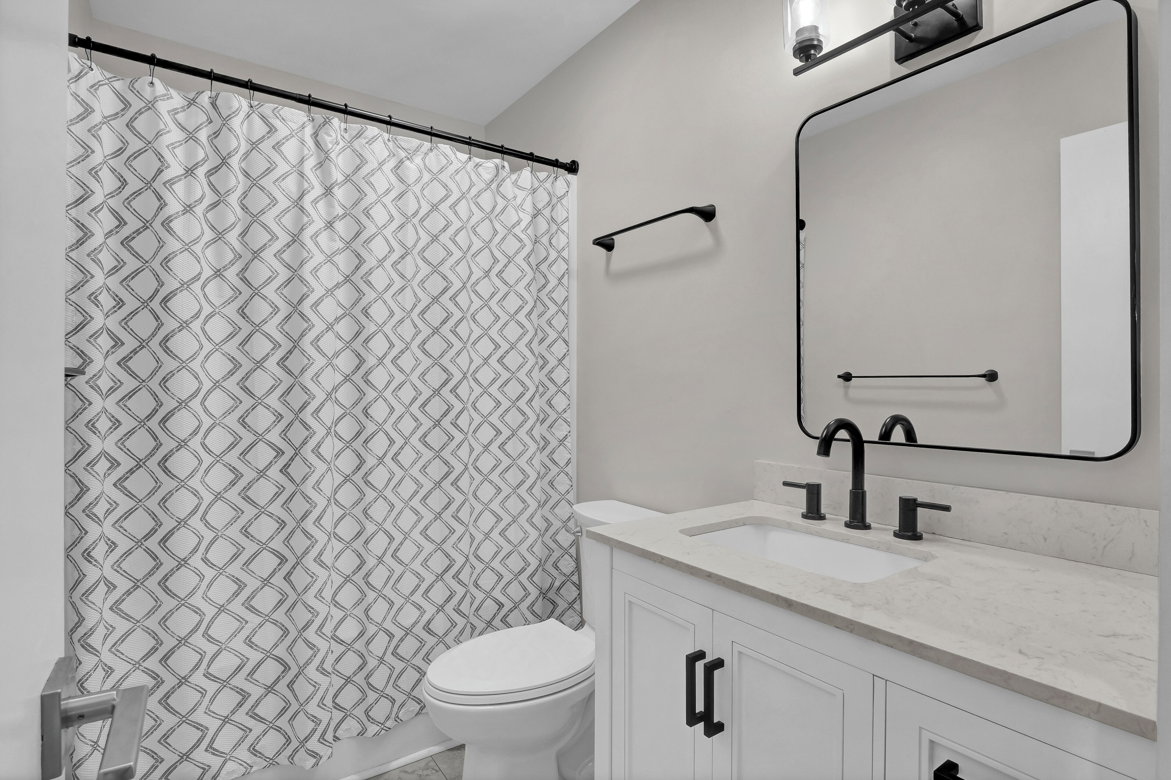 Un baño con cortina de ducha estampada, un inodoro blanco, un lavabo con espejo y un perchero para toallas.