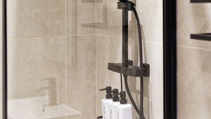 A glass-enclosed shower with a handheld showerhead, a wall-mounted control panel, and a bottle of shampoo. - Boho Vista| Stylish Central1BR Flat in Cardiff Bay (Cardiff)