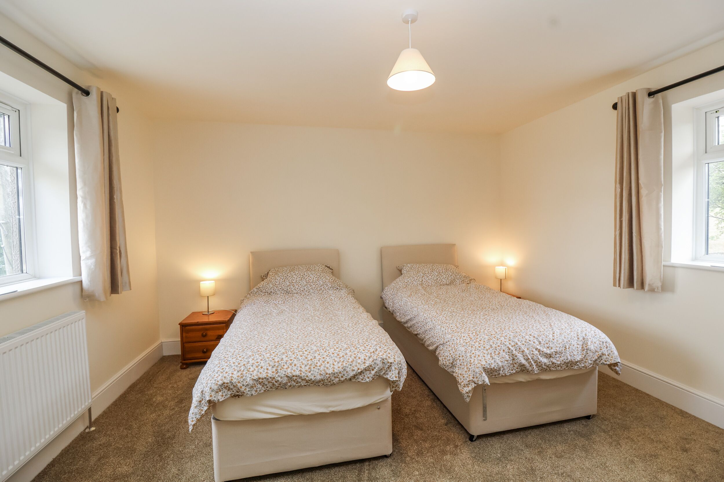 Une chambre avec deux lits simples, une table de chevet, une lampe et une fenêtre avec des rideaux.