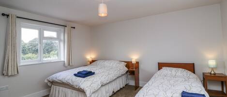 A bedroom with two beds, a window with curtains, a ceiling light, and bedside lamps.