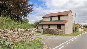 Une maison à deux étages, dotée d’un mur en pierre et d’un toit recouvert de tuiles rouges, située au bord d’une route.
