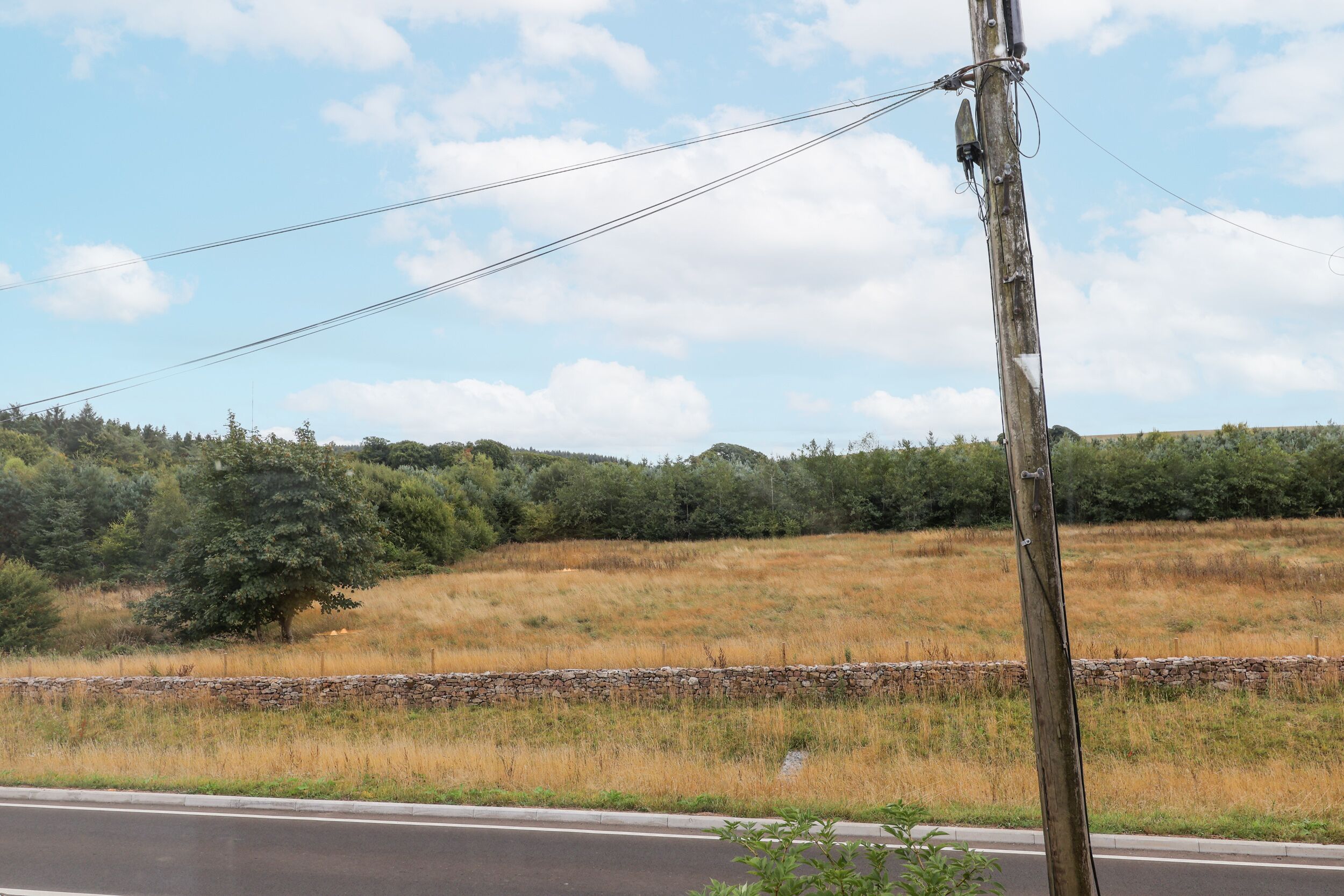 A rural landscape with a stone wall, a road, and a wooden utility pole.