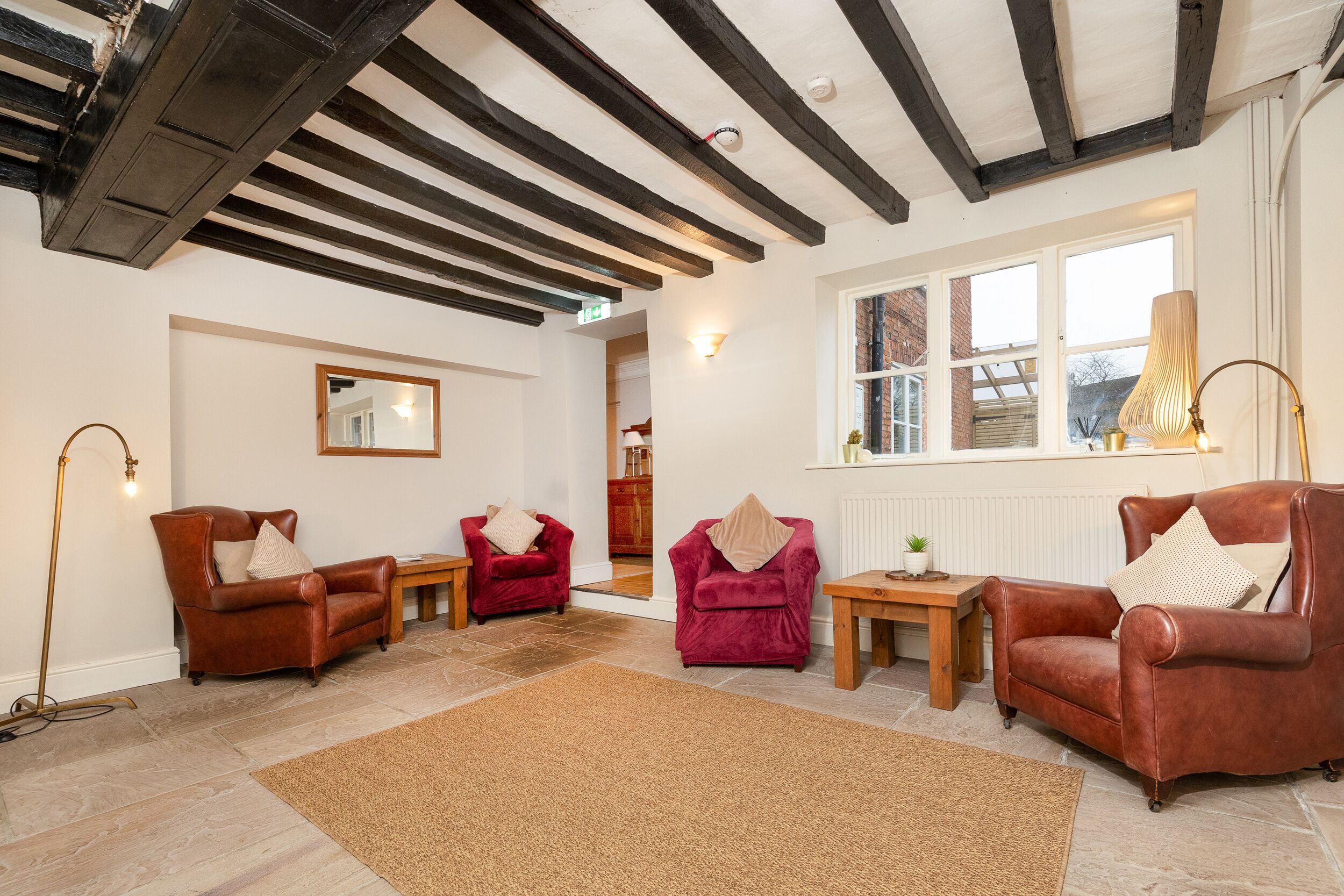 A spacious living room with exposed wooden beams, a large window, and three leather armchairs.