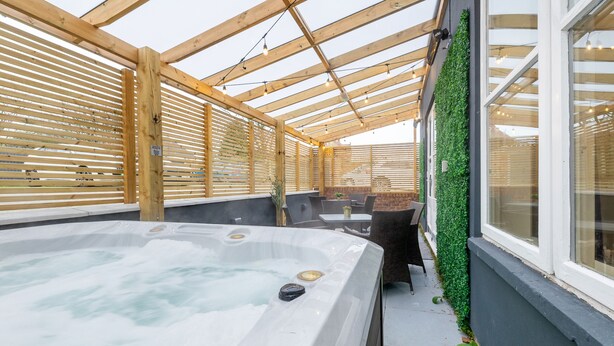 Un bain à remous situé dans un espace extérieur abrité, avec des poutres en bois et un mur végétal.