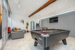 A pool table with balls, a sofa, a potted plant, and a fire extinguisher in a room with a modern design and a wooden ceiling beam. - Hambleton House (Derby)