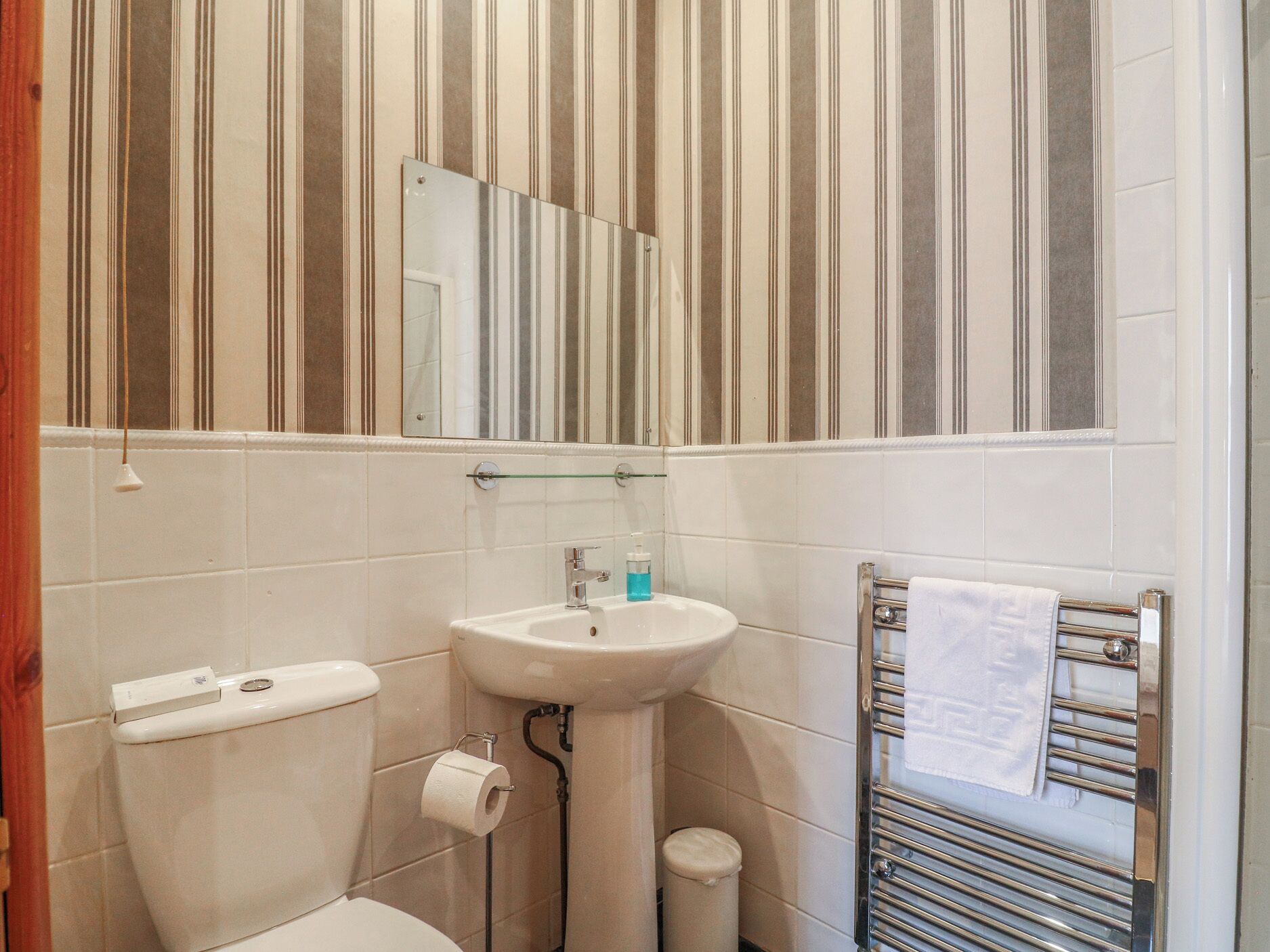 Een badkamer met een gestreepte wand, een wastafel, toilet, spiegel en handdoekrek.
