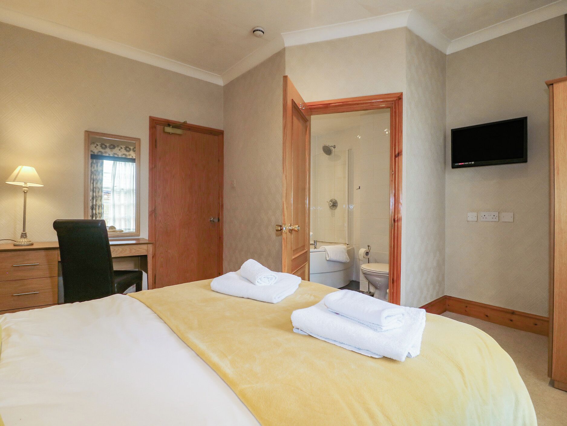 A hotel room with a bed, a desk, a chair, a TV, a shower, and a toilet.