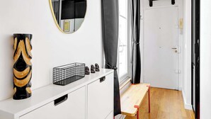 A modern room with a white vanity, a mirror, a black abstract sculpture, a black wire basket, and a wooden bench. - Chic 1BR in the Heart of Le Marais (Paris)