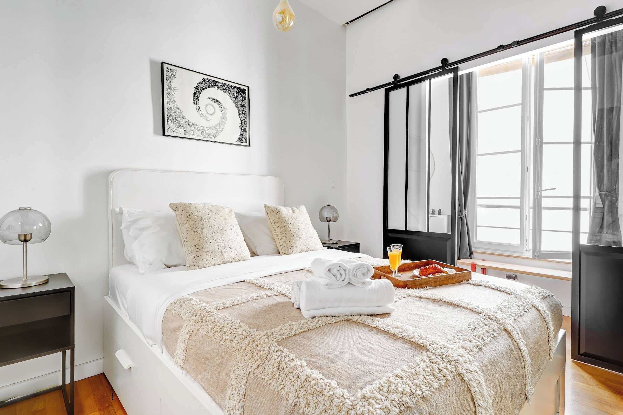 A neatly arranged bedroom with a bed, a bedside table, a tray with a glass of orange juice, and a framed artwork on the wall.