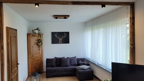 A living room with a dark sofa, a wooden cabinet, a painting of a deer, and a window with sheer curtains. - Vacation home Schmidt with Nicole and Frank (Oberzent)
