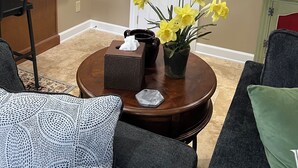 A living room with a round coffee table, two armchairs, a small side table with a tissue box, and a vase with yellow flowers. - Beautiful townhome in the village of Banner elk It doesn’t get better than this. (Banner Elk)