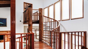 A wooden spiral staircase with a wooden railing, a wooden bench, and a welcome mat at the bottom.