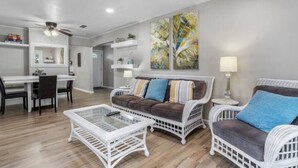 Un salon moderne avec un canapé en osier blanc, une table basse en verre et un coin repas comprenant une table et des chaises blanches.