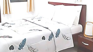 Une chambre d’hôtel comprenant un lit, une table de chevet, une commode, une fenêtre avec des rideaux et un appareil de climatisation.