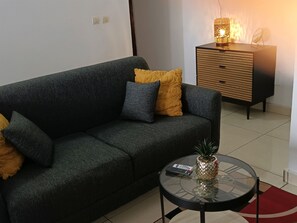 Una sala de estar moderna con un sofá verde oscuro, una mesita redonda con un centro de mesa de piña y un aparador de madera con una lámpara.