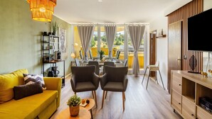 A modern living room with a sofa, two armchairs, a dining table with chairs, a TV, and a bookshelf. - Apartment 'Superior 238' with Mountain View, Shared Garden, and Wi-Fi (Braunlage)