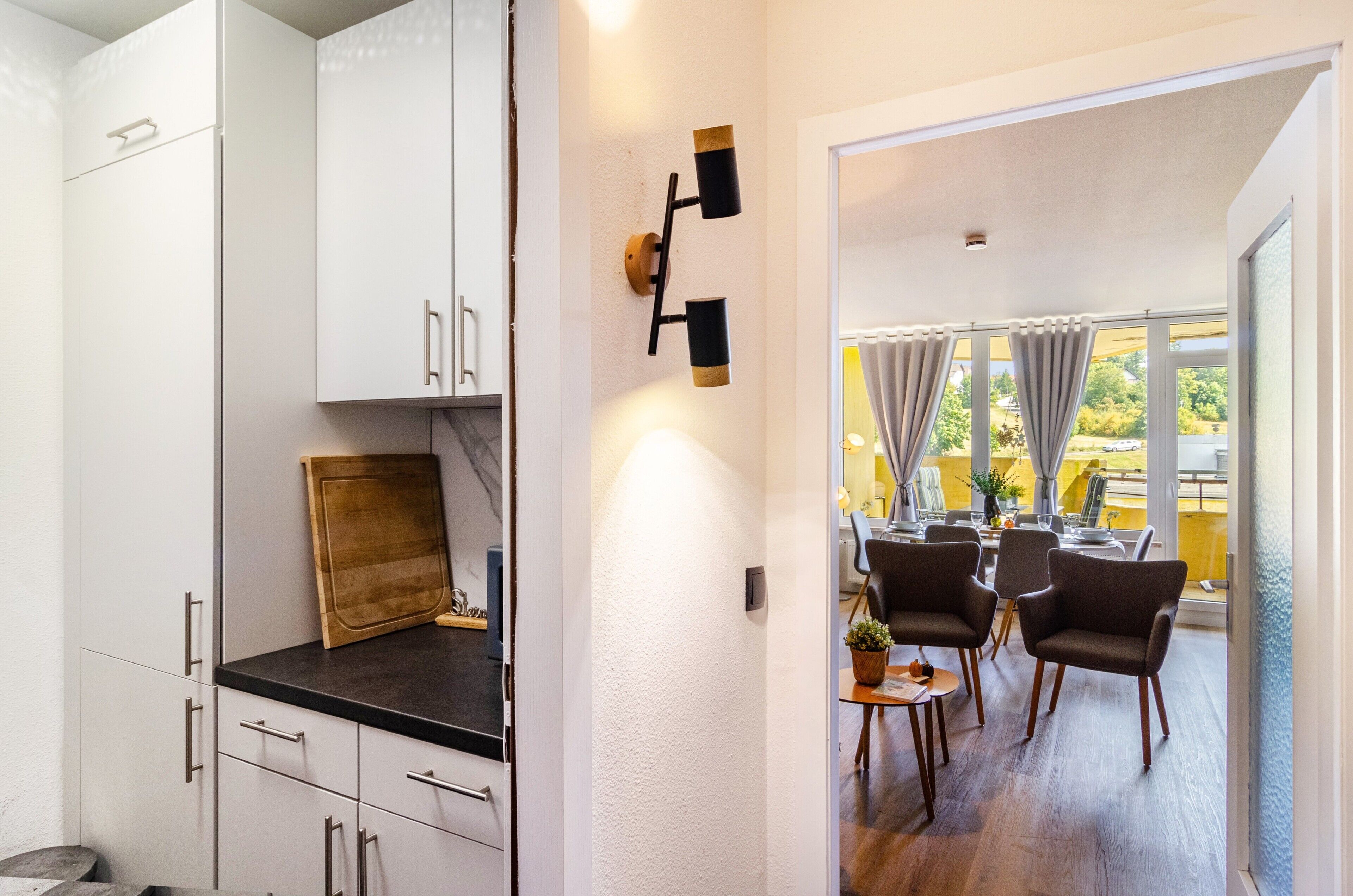 A modern kitchen with white cabinets, a wooden cutting board, and a dining area with a table and chairs.