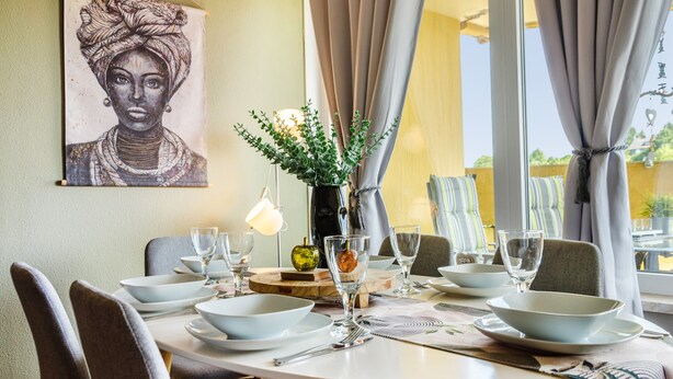 A dining area with a round table set for four, a vase with green plants, and a painting on the wall. - Apartment 'Superior 238' with Mountain View, Shared Garden, and Wi-Fi (Braunlage)