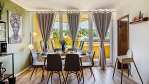 A dining area with a table set for four, chairs, a vase with flowers, and a view through large windows. - Apartment 'Superior 238' with Mountain View, Shared Garden, and Wi-Fi (Braunlage)