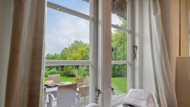 A room with a large window, a chair, a table, and a towel. - Holiday Home 'Deichkate' – Vacation in a Historic Monument with Panoramic Views (Dagebüll)