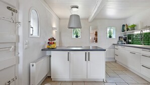 A modern kitchen with white cabinets, a central island, a hanging light fixture, and a window with a view of greenery. - Holiday Home 'Deichkate' – Vacation in a Historic Monument with Panoramic Views (Dagebüll)