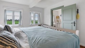 A bedroom with a bed, a window, a door, and a tennis racket on the wall. - Holiday Home 'Deichkate' – Vacation in a Historic Monument with Panoramic Views (Dagebüll)
