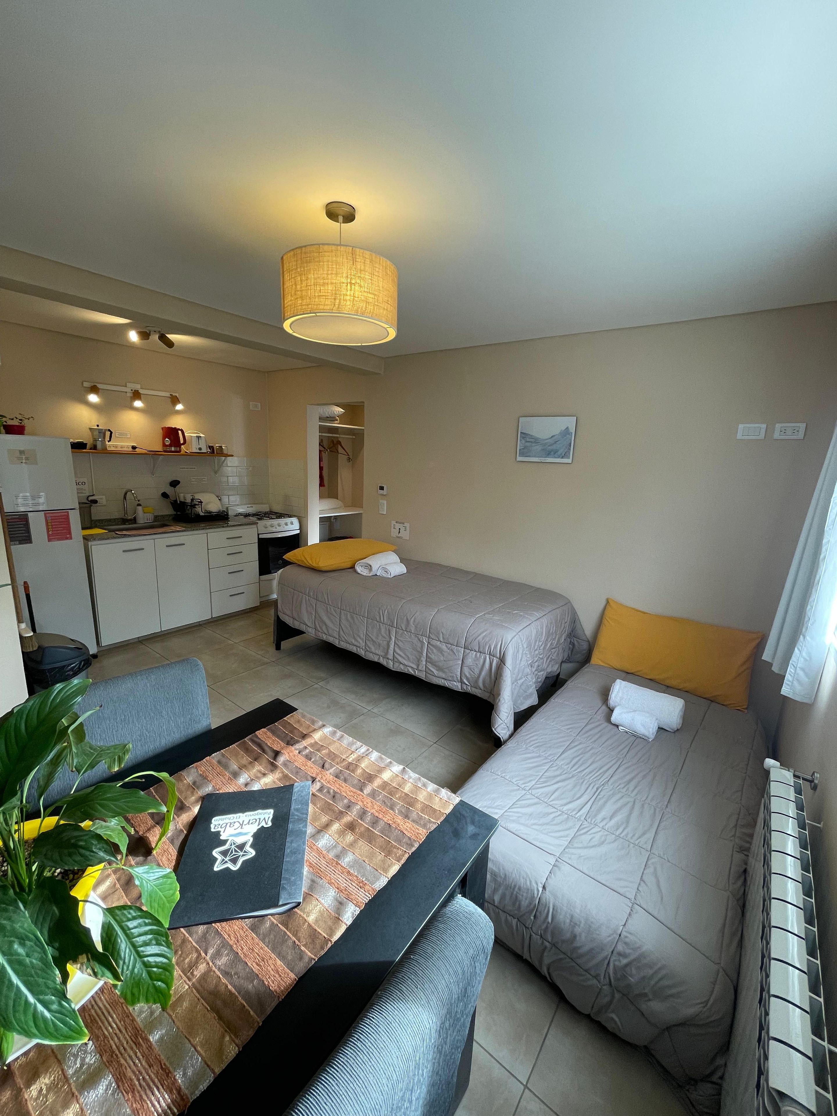 A compact room with a kitchenette, a dining area, and two beds with towels.