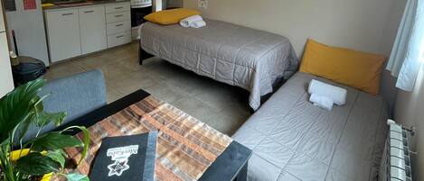 A compact room with a kitchenette, a dining area, and two beds with towels.