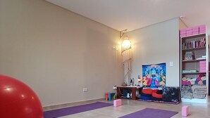 A spacious room with a large exercise ball, purple mats, a colorful painting, and a bookshelf. - MerKaba Aparts (El Chalten)