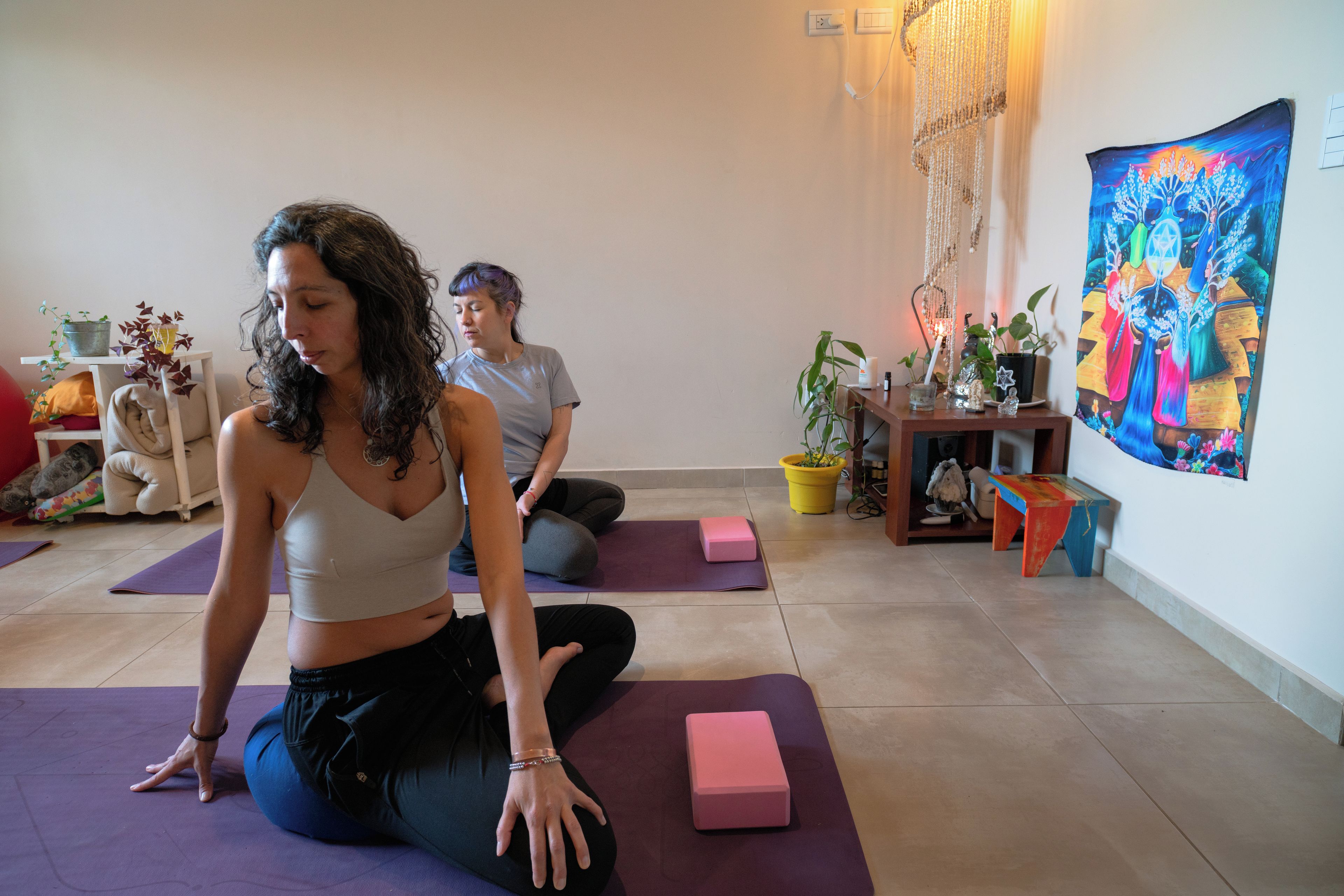 Dos personas practicando yoga sobre esterillas moradas en una habitación con un cuadro grande y colorido en la pared.