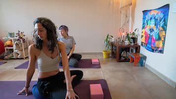 Dos personas practicando yoga sobre esterillas moradas en una habitación con un cuadro grande y colorido en la pared.