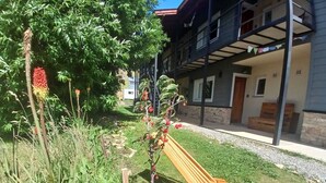 A garden with a wooden bench, a small tree with red berries, and a building with balconies. - MerKaba Aparts (El Chalten)