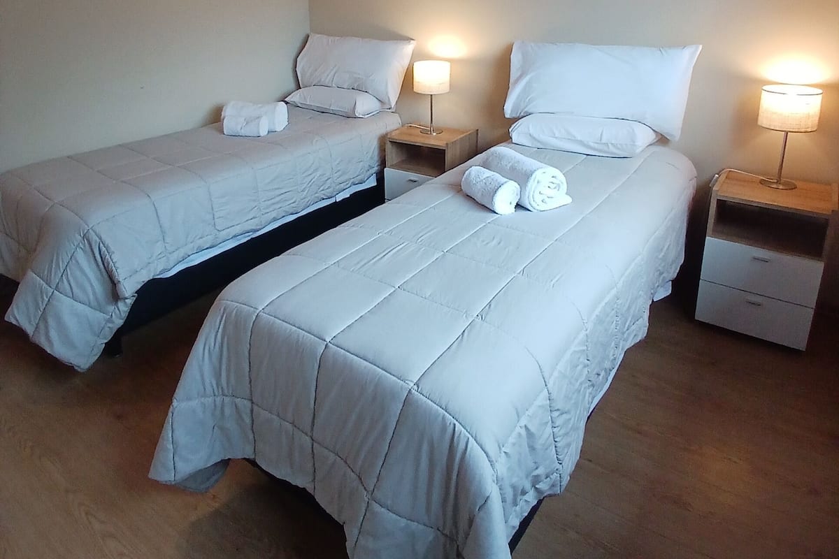 Une chambre avec deux lits simples, chacun doté d’une table de chevet et d’une lampe. La chambre est pourvue d’un plancher en bois et d’un plafond en pente.