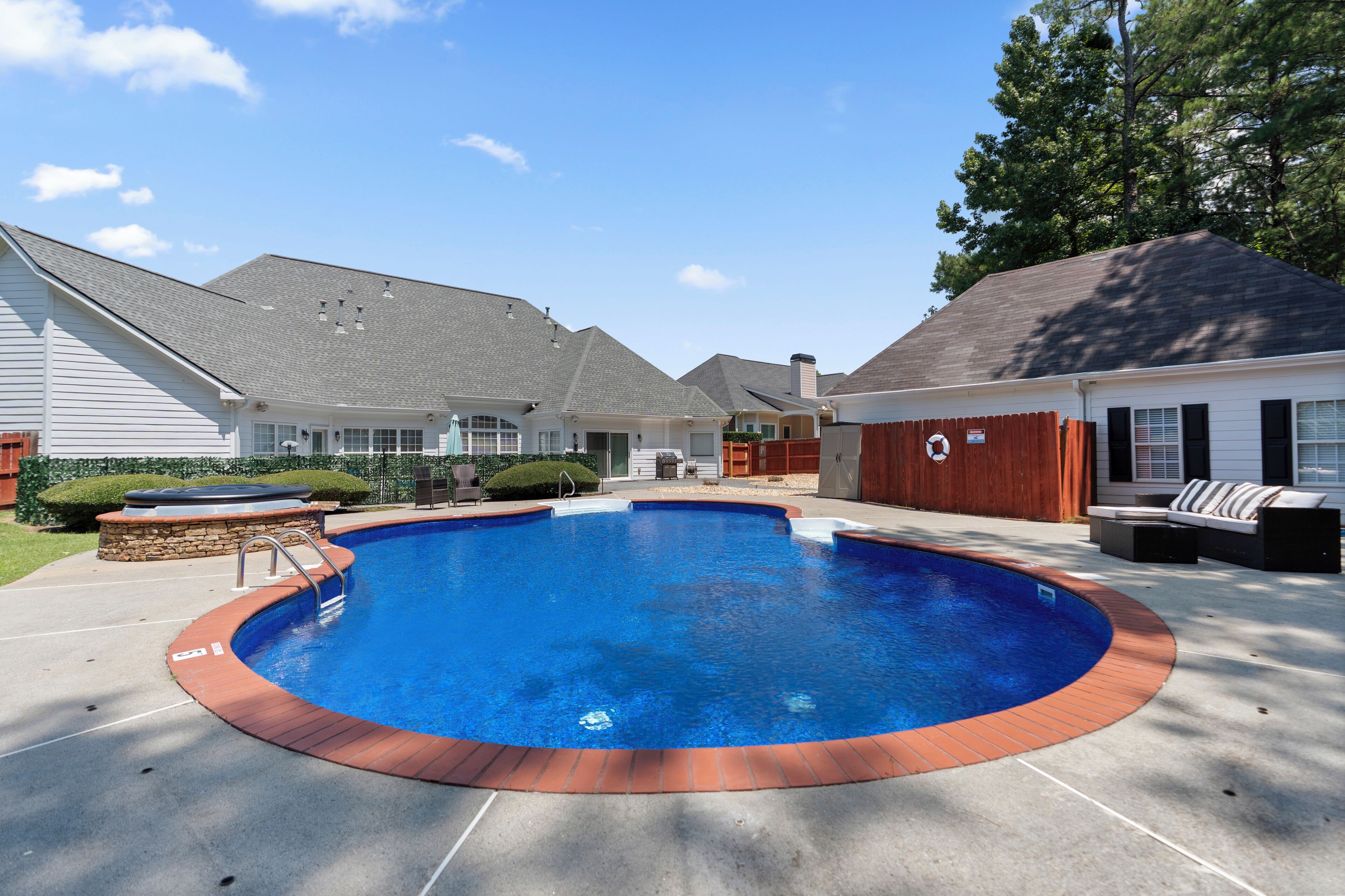 A backyard with a swimming pool, a hot tub, and a patio area with outdoor furniture.