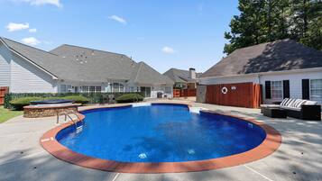 A backyard with a swimming pool, a hot tub, and a patio area with outdoor furniture.