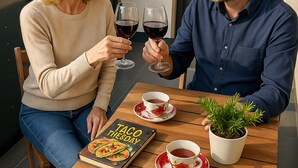 Dos personas sentadas en una mesa de madera al aire libre, con un libro que dice "Taco Tuesday" y una planta en maceta.